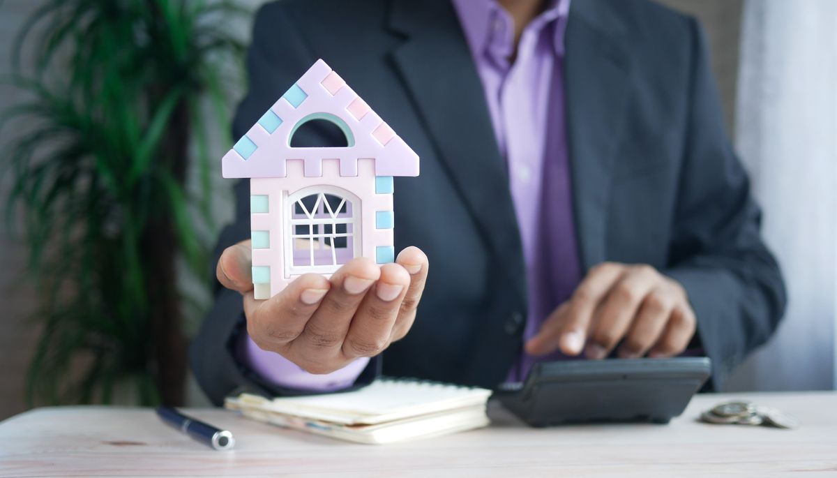 Professional holding a house model beside a calculator