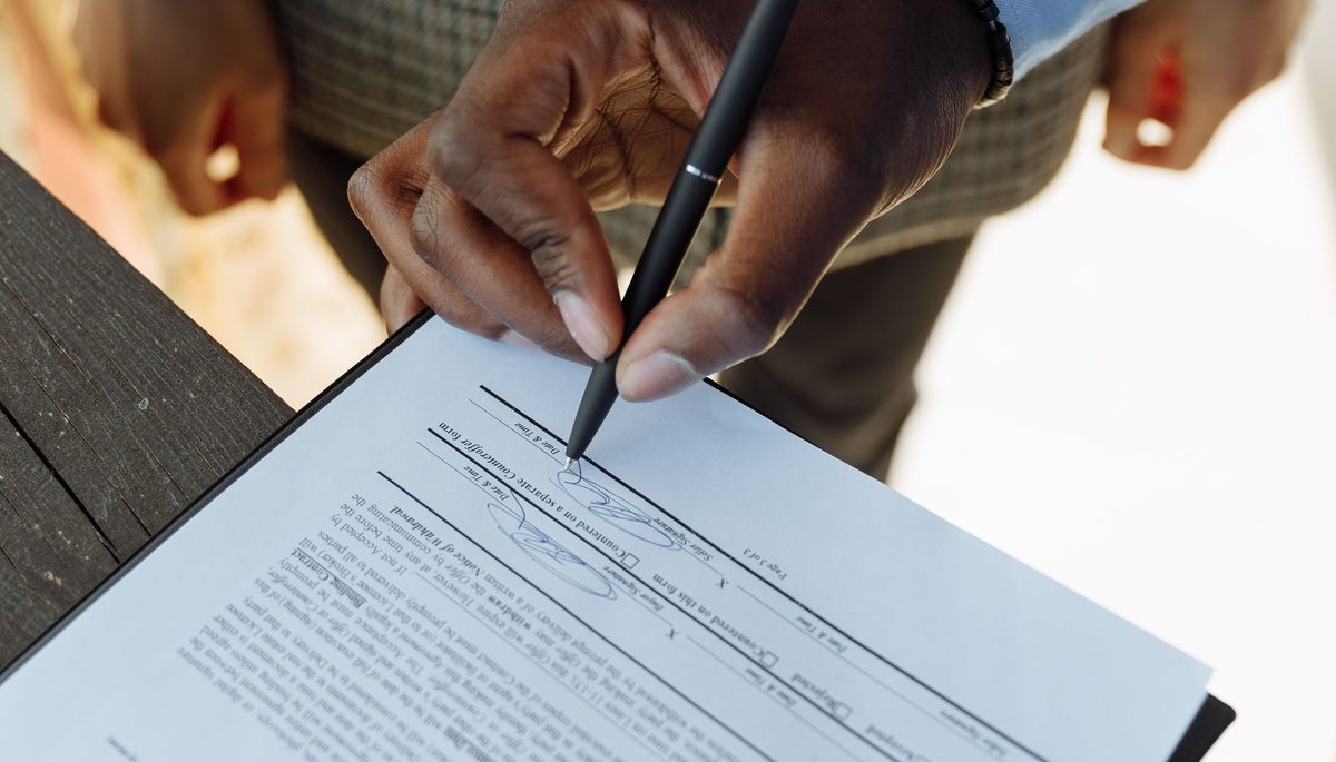 Person signing a printed contract outdoors