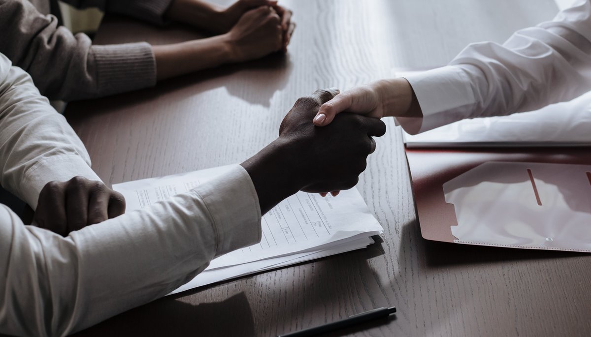 Two people shaking hands over documents at a desk