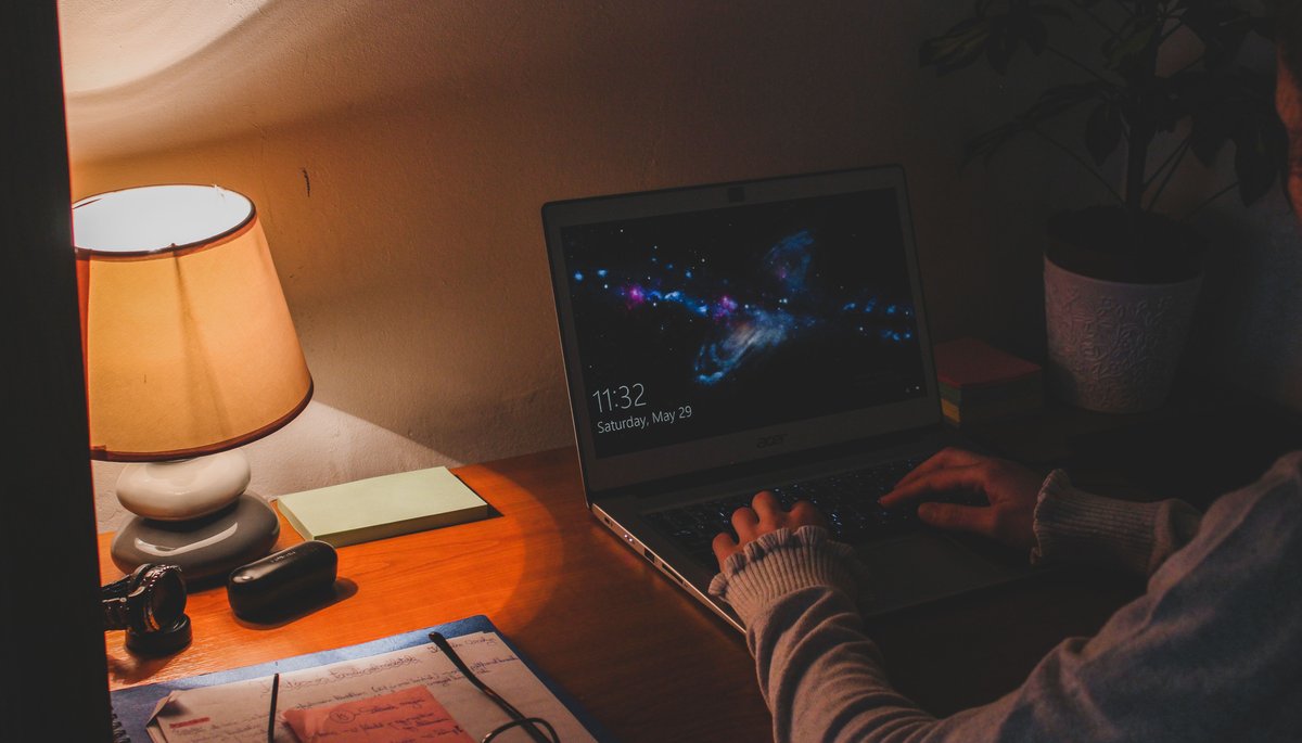 Person working on a laptop at night under a warm desk lamp